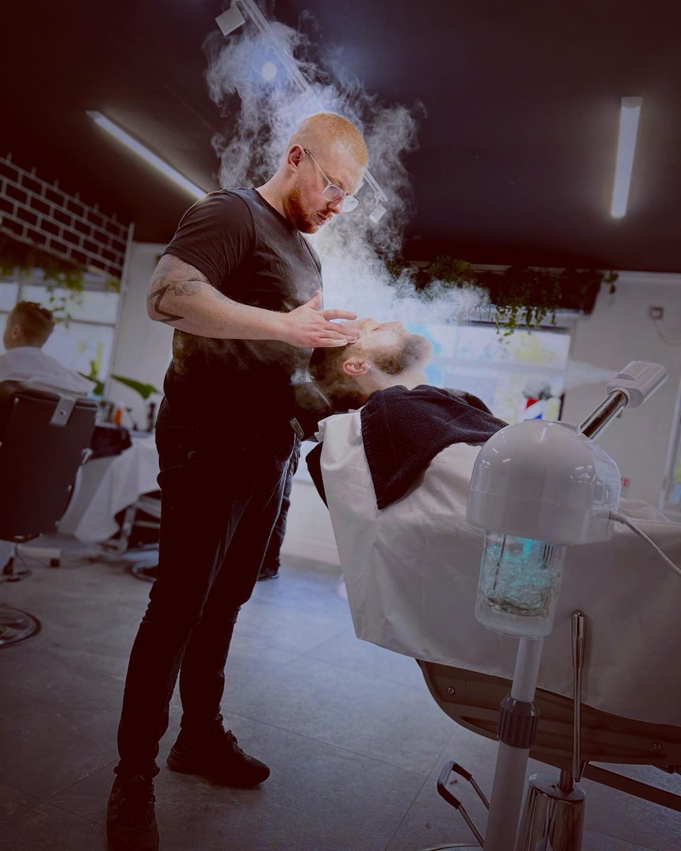 A barber giving a hot towel treatment, steam rising from the towel