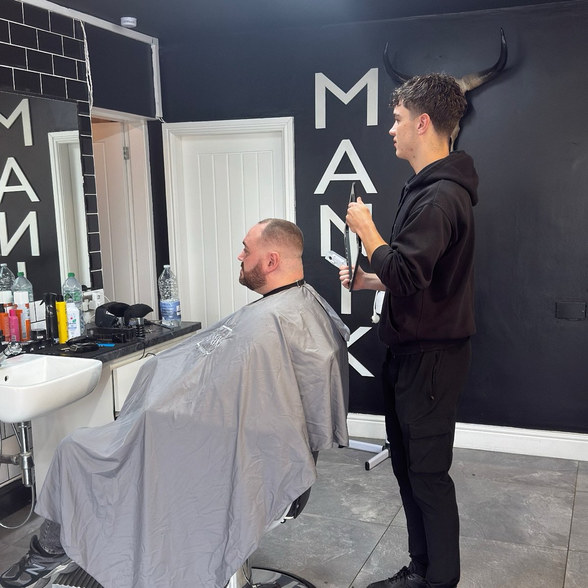 Barber cutting a client's hair in front of the MANIK wall